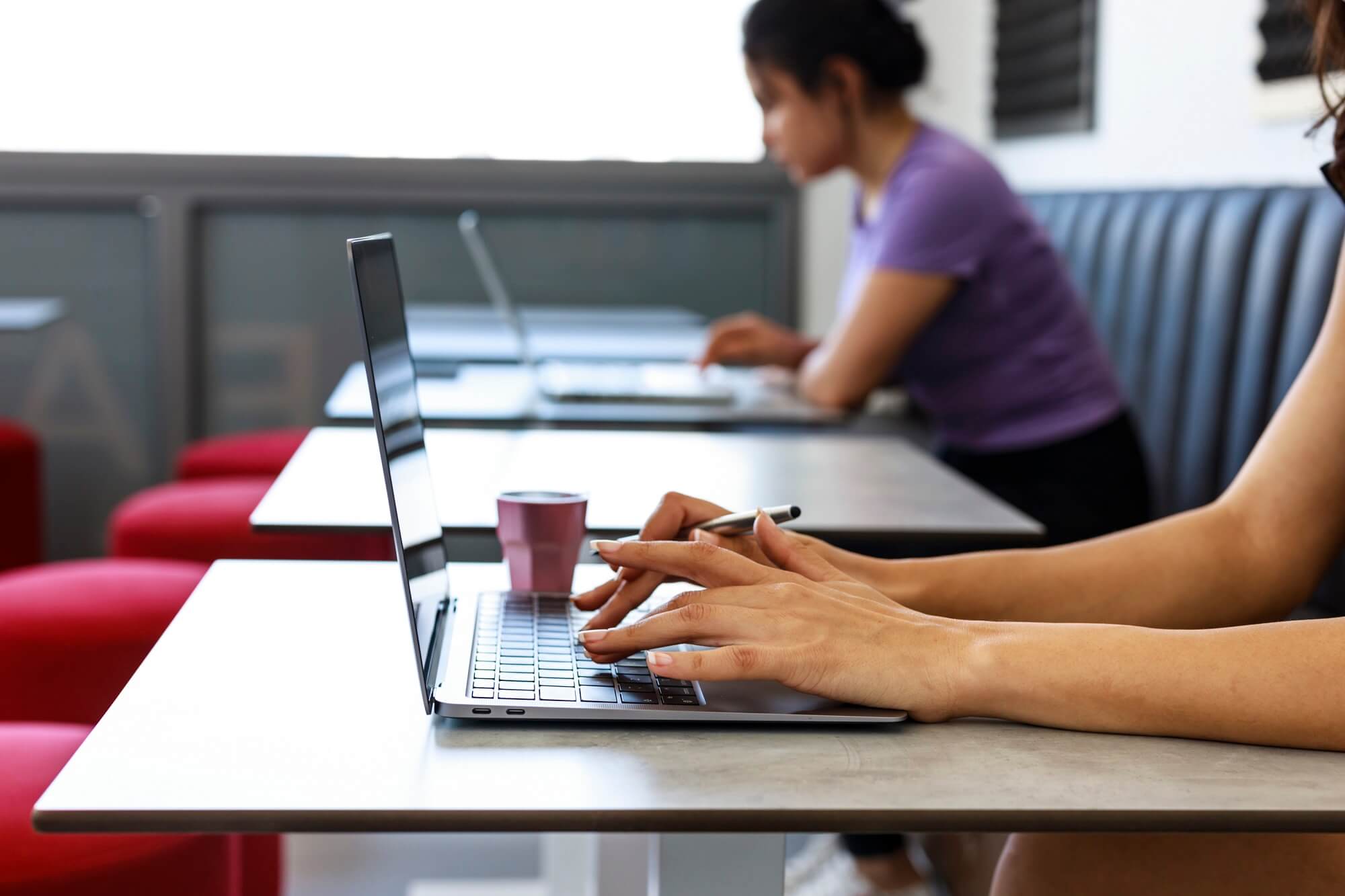 Member working on a laptop at a shared table in the hub
